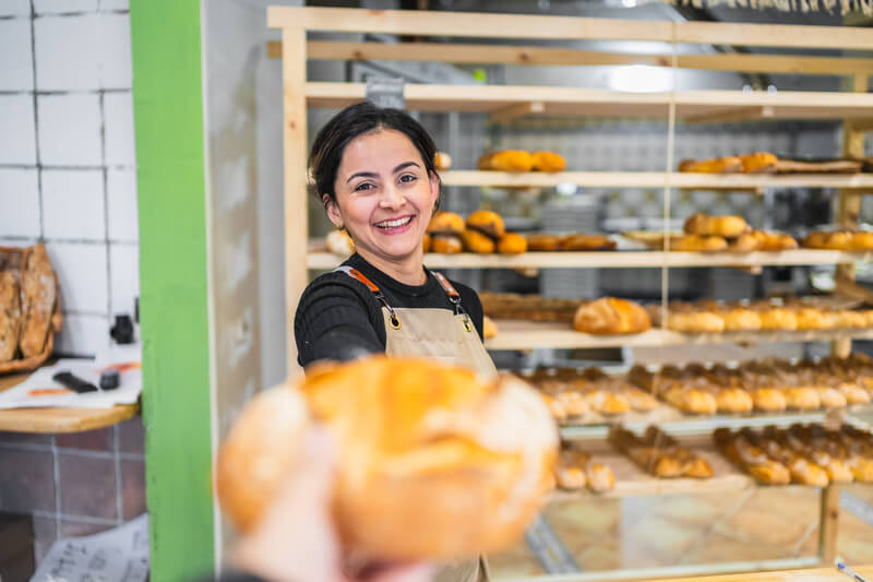 Smiling baker offering freshly baked bread in bakery shop